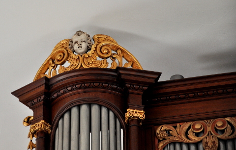 Les deux angelots des couronnements ont une expression différente.
Celui de droite chante avec un air très concentré.
Celui de gauche (ici représenté) a une expression plus réjouie.