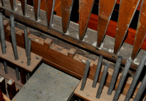 Le bas du revers de la façade.
En haut, le revers des faux tuyaux en bois (plats de ce coté).
On distingue des bancs de la nef en transparence.
Au pied de chaque planche constituant un faux tuyau,
on trouve le trou dans le bois, où venait se fixer le postage
permettant d'alimenter les tuyaux de façade du temps de l'orgue Wetzel.
En bas, les aigus de deux jeux. (La Flûte majeure en bois à gauche.)
Entre les tuyaux du fond et la façade, on remarque une pièce en bois
munie de créneaux et de mortaises : cela pourrait être le support
des jalousies d'une boîte d'expression disparue en 1959.