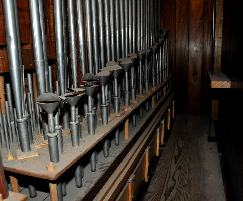 Une vue sur la tuyauterie de la pédale.
Le récit est à droite, la façade vers la gauche (invisible).
On regarde vers la gauche de l'instrument.
Les tuyaux en bois au fond, à gauche, appartiennent à la Soubasse.
La Flûte 8' et le Prestant sont hors champ, mais on voit à gauche,
quelques notes de la Mixture 3 rangs. En revenant vers la droite,
il y a la grande Douçaine 16' (avec des faux-sommiers renforcés),
et, au premier plan, le Chalumeau 4', avec ses résonateurs en double
cône, dont le supérieur est très évasé, et muni d'un opercule.