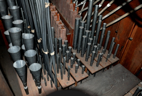 Une vue sur la moitié droite (Cis) de la tuyauterie du grand-orgue.
Le fond de l'instrument se trouve à gauche, et la façade à droite.
De gauche (passerelle) à droite (façade) :
la Trompette (6 tuyaux sont harmoniques, de longueur double ; avec les 6 de l'autre côté,
cela représente la dernière octave (gis''-g''') complète),
la Flûte conique 4', les postages de la Cymbale et du Cornet (postés en hauteur,
et que l'on verra sur l'image suivante), le Salicional, le Bourdon 8',
le Bourdon 16' (les tuyaux aigus des deux bourdons sont en métal)
le Prestant, et la Montre 8'. En bas à droite, on distingue
deux tuyaux du Bourdon 16' de l'autre moitié du grand-orgue ("C").